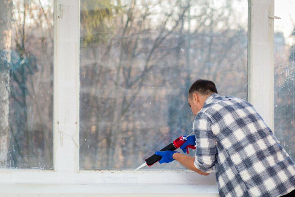 Davofrío - Eficiencia Energética - Hombre sellando una ventana con silicona para evitar fugas de aire